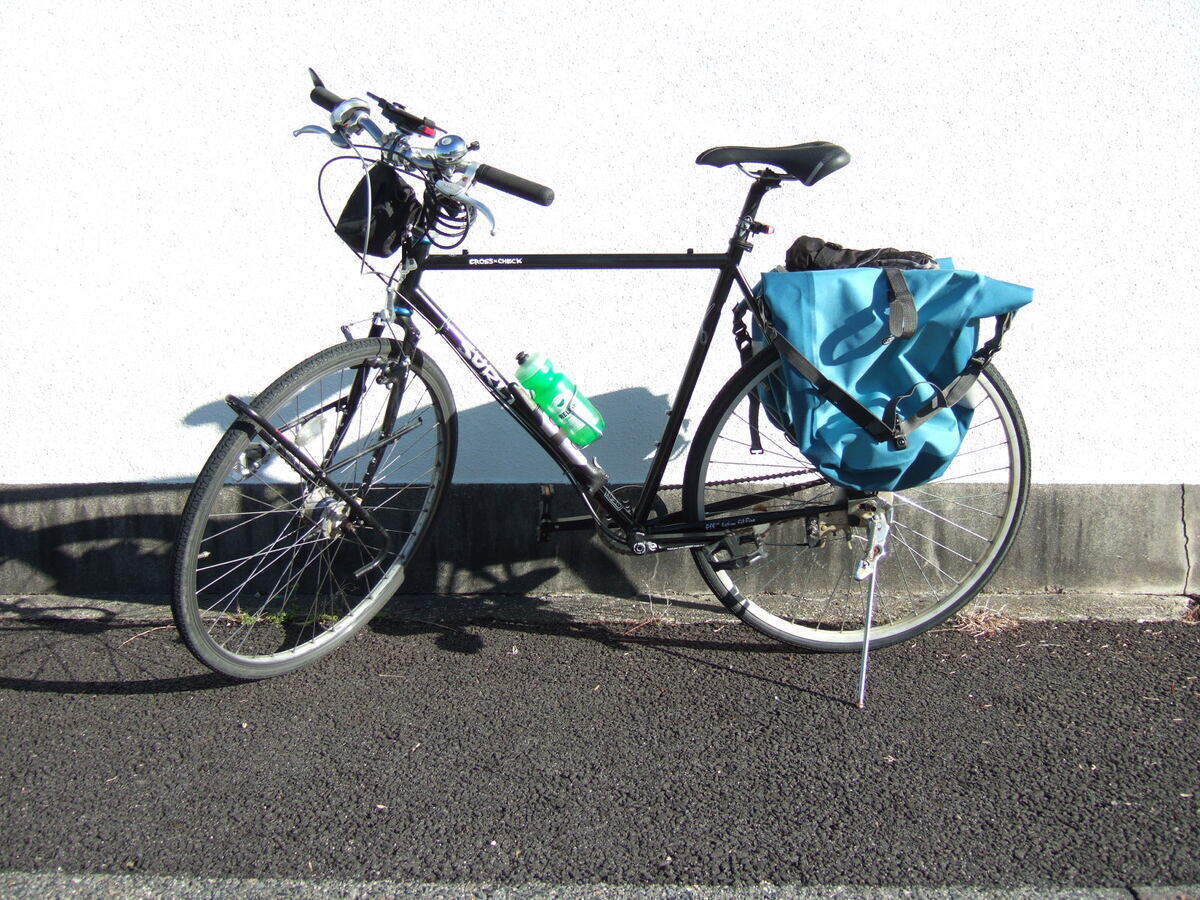 A bicycle with rear panniers parked in front of a plain white stucco wall