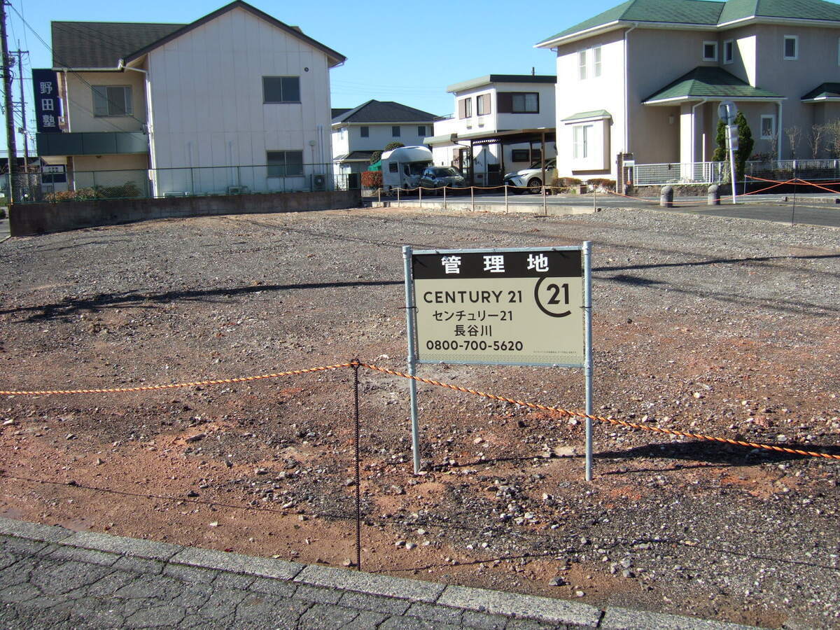 A sign standing in an empty lot reads (in English translation) “Under management / Century 21” above the name of the estate agent and a phone number.