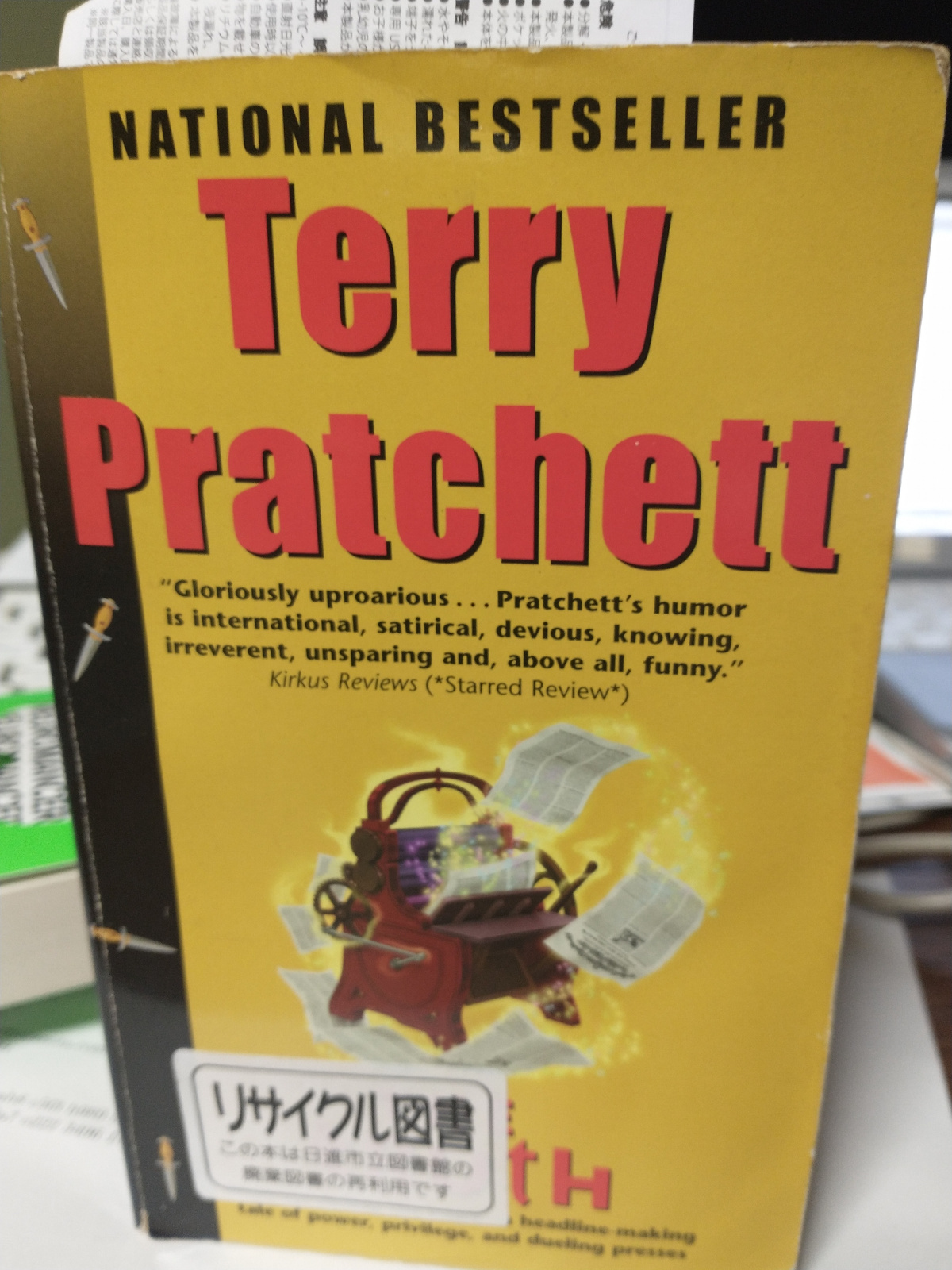 A copy of “The Truth,” a novel by Terry Pratchett, with a sticker over the title reading (in English translation): “Recycle Book/This is a book for reuse, culled from the Nisshin City Library