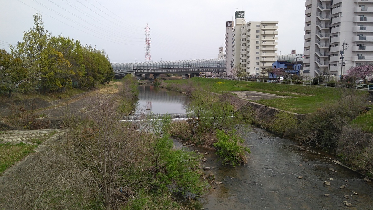 A view from a bridge, looking east along the Tenpaku River. A thoroughfare enclosed in a sound-dampening shroud spans the river in the distance.