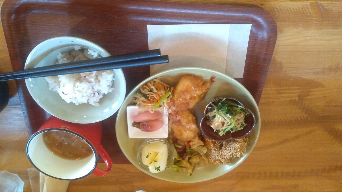 A lunch plate with: a salad of grilled tofu, sprouts and shimeji mushrooms; braised pumpkin squash rolled in sesame; fried vegetables; apple slices; pickled myōga; pickled lotus root, carrot, and cucumber salad; and chicken tatsuta-age with miso soup and hot coffee