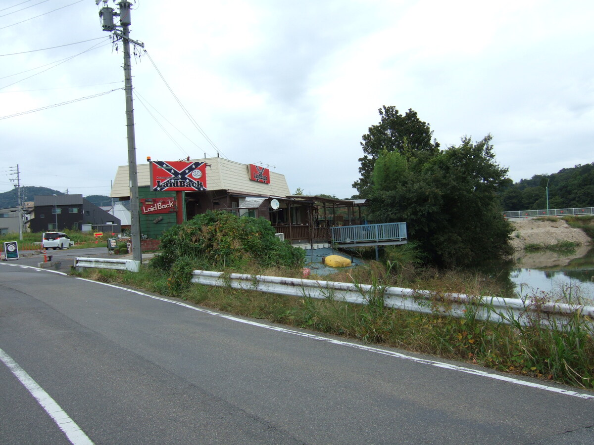 A one-story building behind a rusting guardrail, with a patio fronting onto a large pond. A large Confederate flag is emblazoned on the side of the building.