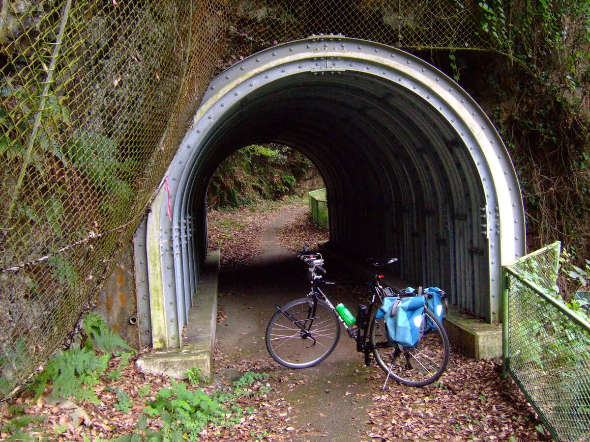 A bicycle parked in the archway of a small tunnel through a rocky outcropping.