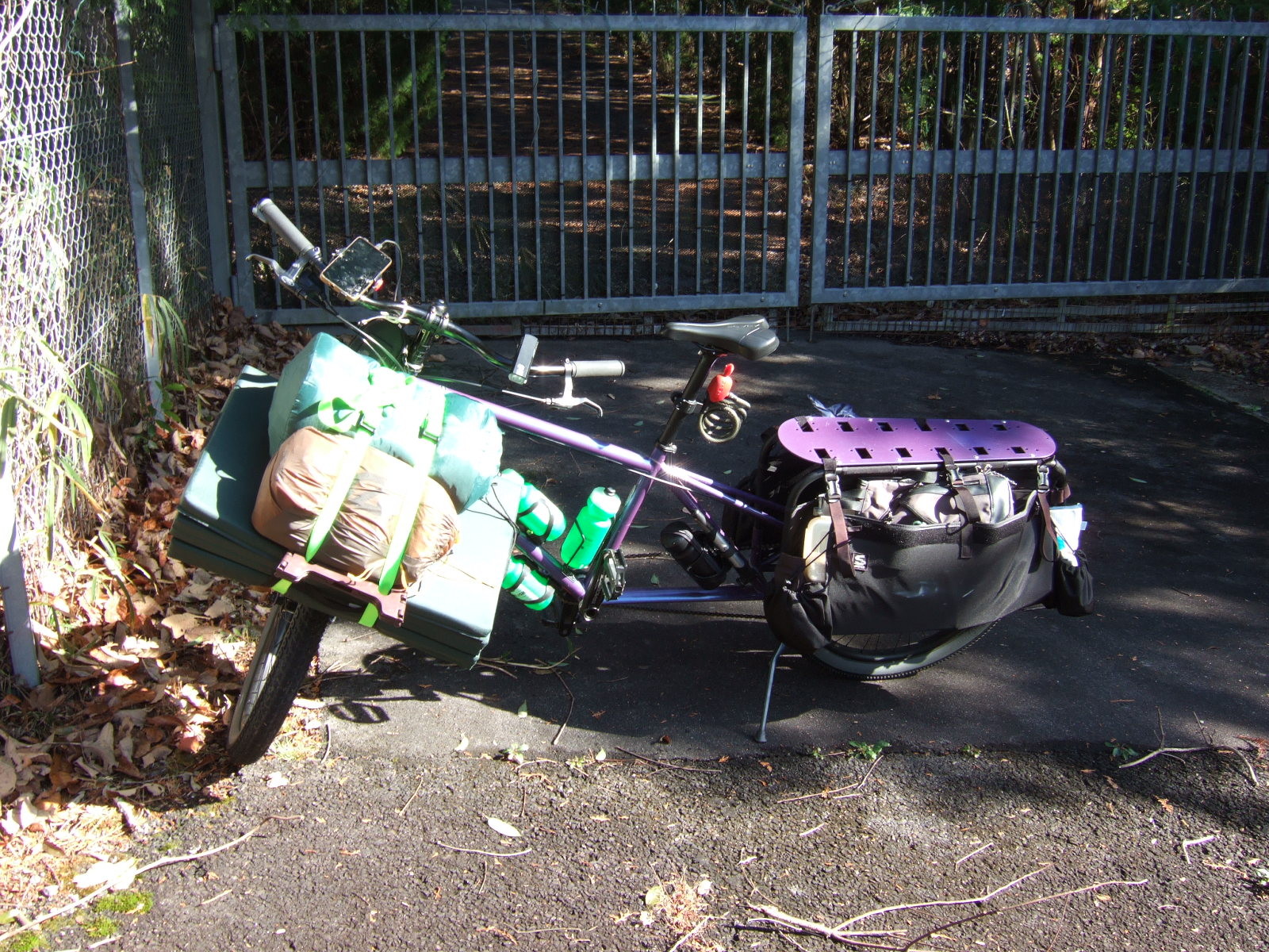 A loaded cargo bike parked in front of a locked steel gate.