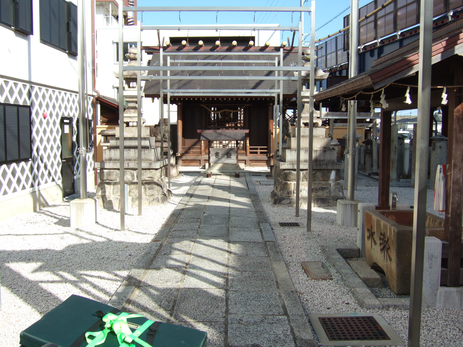 A view of the walkway mentioned in the other photo description, but looking back after climbing the steps, turning left, and passing through again to the street. A small shrine is visible at the end of the walkway, behind some construction scaffolding.