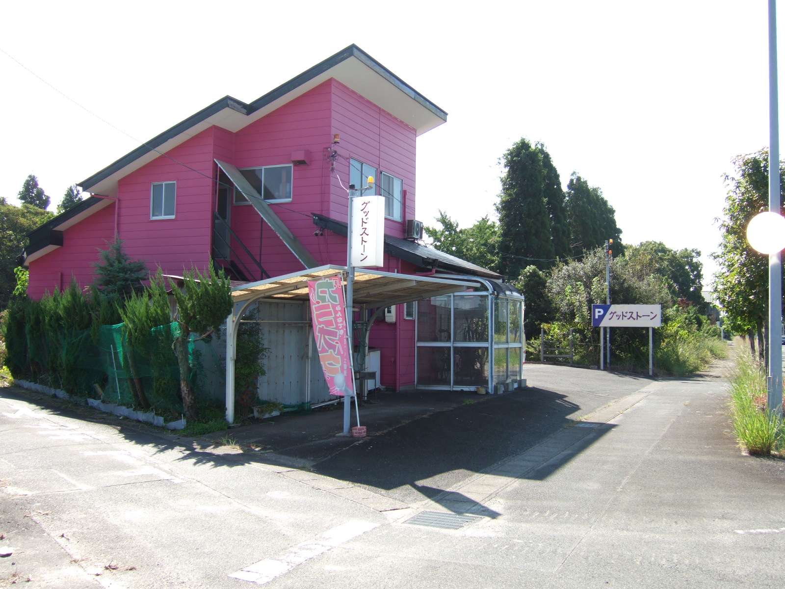 A simple wooden building painted bright pink, surrounded by a parking lot, with some trees beyond.