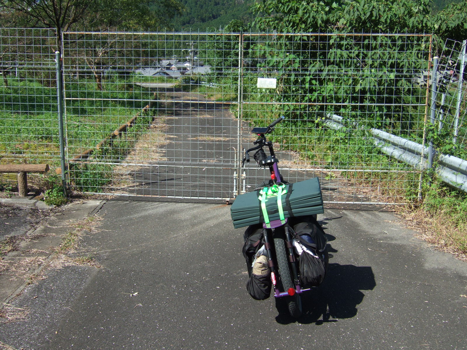 A faded sign reading: “Wildlife diversion gate/You may pass, but be certain to close the gate after you” 動物よけの門扉です・通行は可能ですが通った後必ず閉めてください・よろしくおねがいします\n\nThe sign is decorated with illustrations of a wild boar and a monkey.