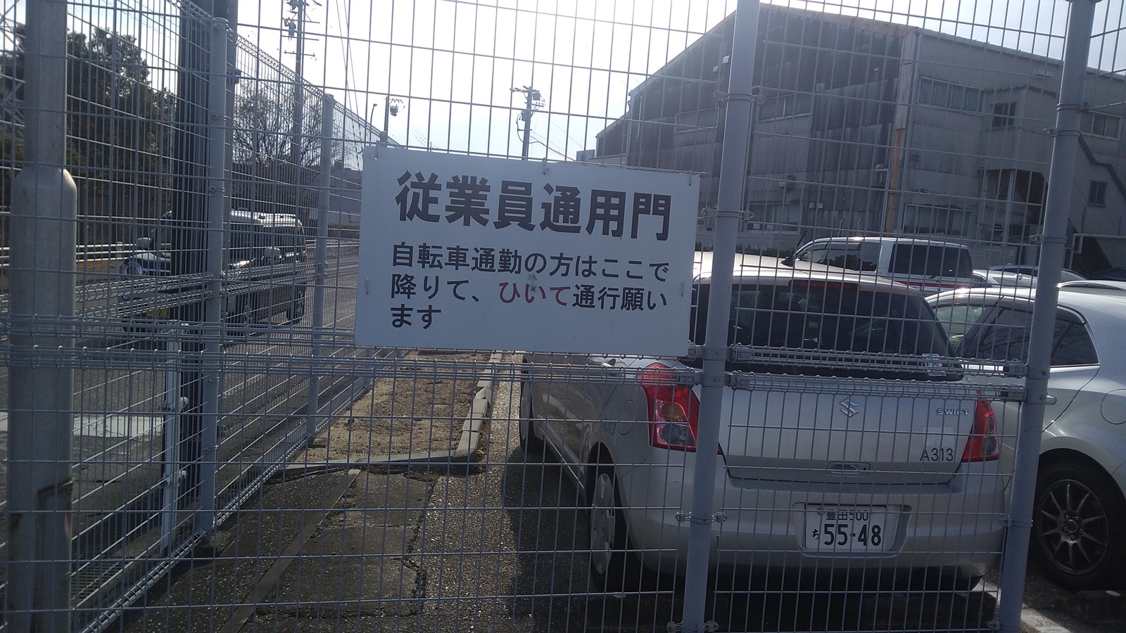 A sign reading (in English translation) “Employee Entry Gate / Those commuting by bicycle are asked to dismount and walk their bikes from this point.”