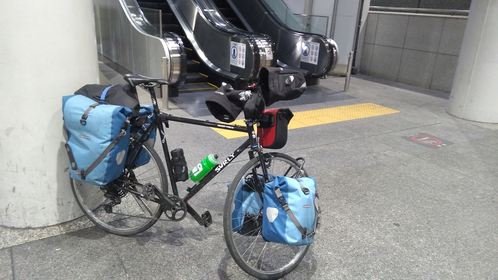 A loaded touring bicycle parked in front of a set of escalators.