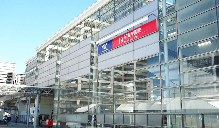 Glassed-in facade of a two-story station building, mounted with a sign reading (in translation): Kenkyūgakuen Station.