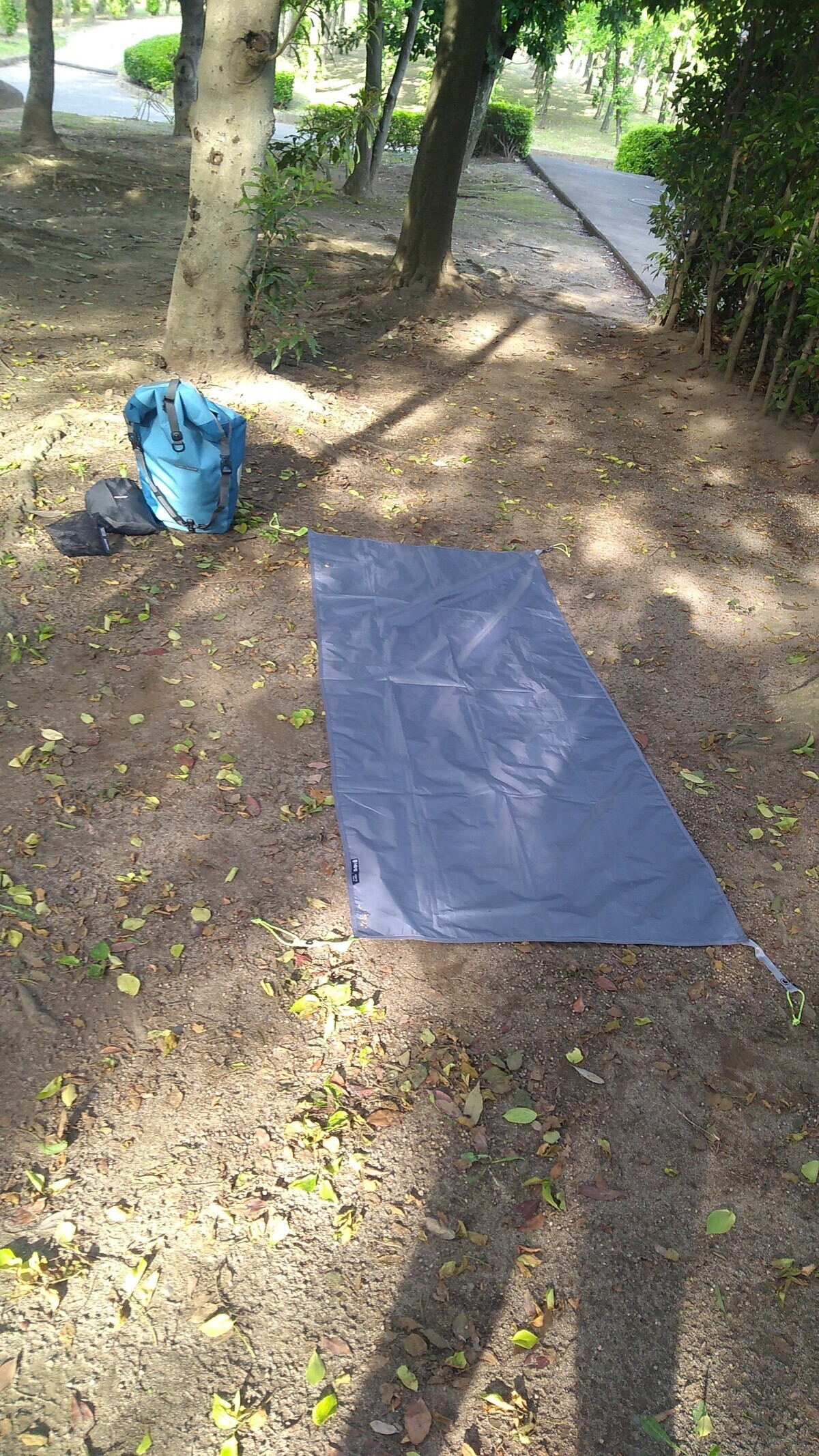 The ground sheet of a one-man tent spread under a tree, with a pannier bag next to it. The shadow of the person taking the picture (me) is visible on the ground.