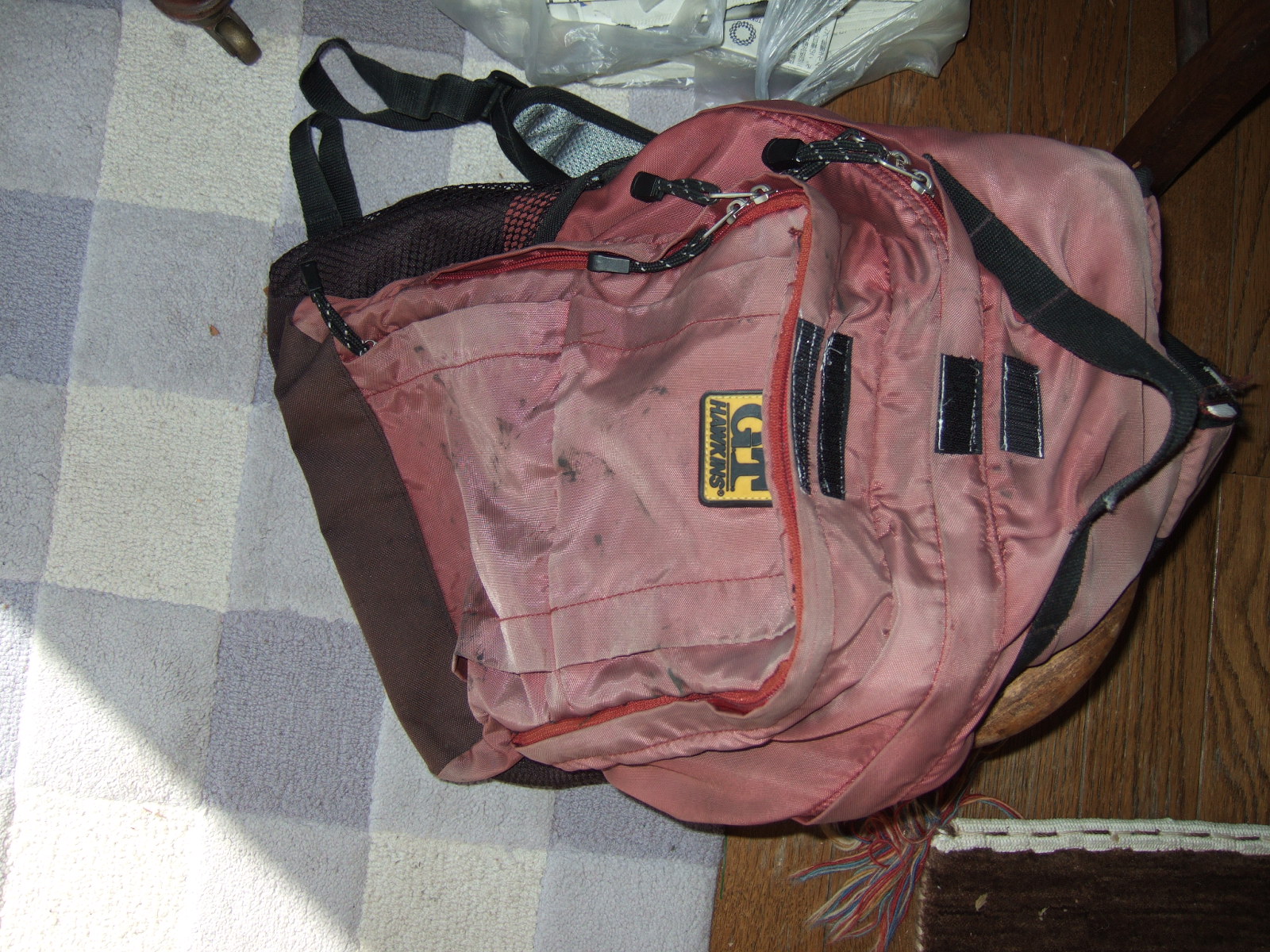 A backpack with its two large pockets zipped shut, revealing a pair of velcro tabs, one on the rain flap and one on the bag-side of the rain flap of each.