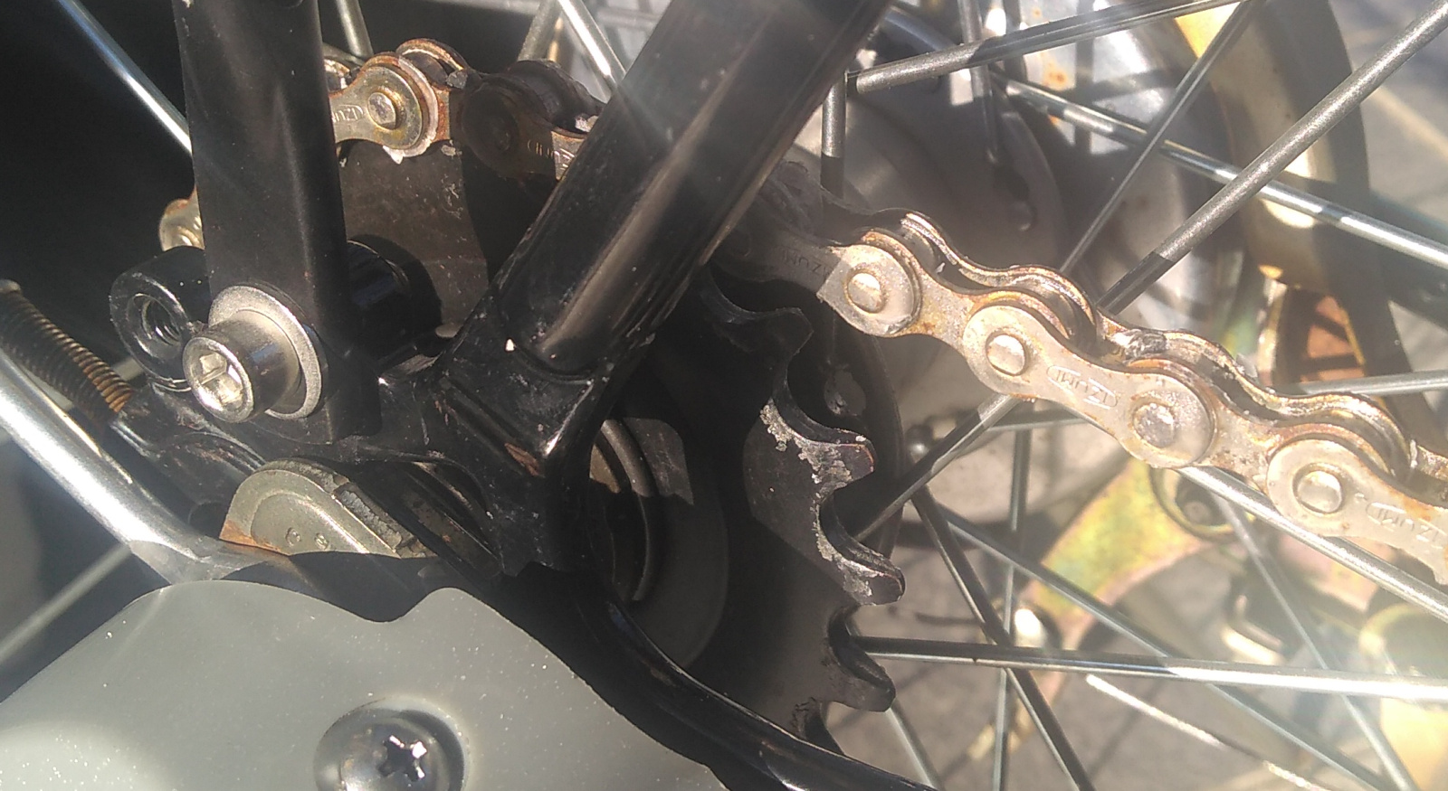 A close-up of the assembled rear sprocket, chain, gearshift mechanism and rear stays of a three-speed bicycle. The sprocket in this view has 21 teeth.