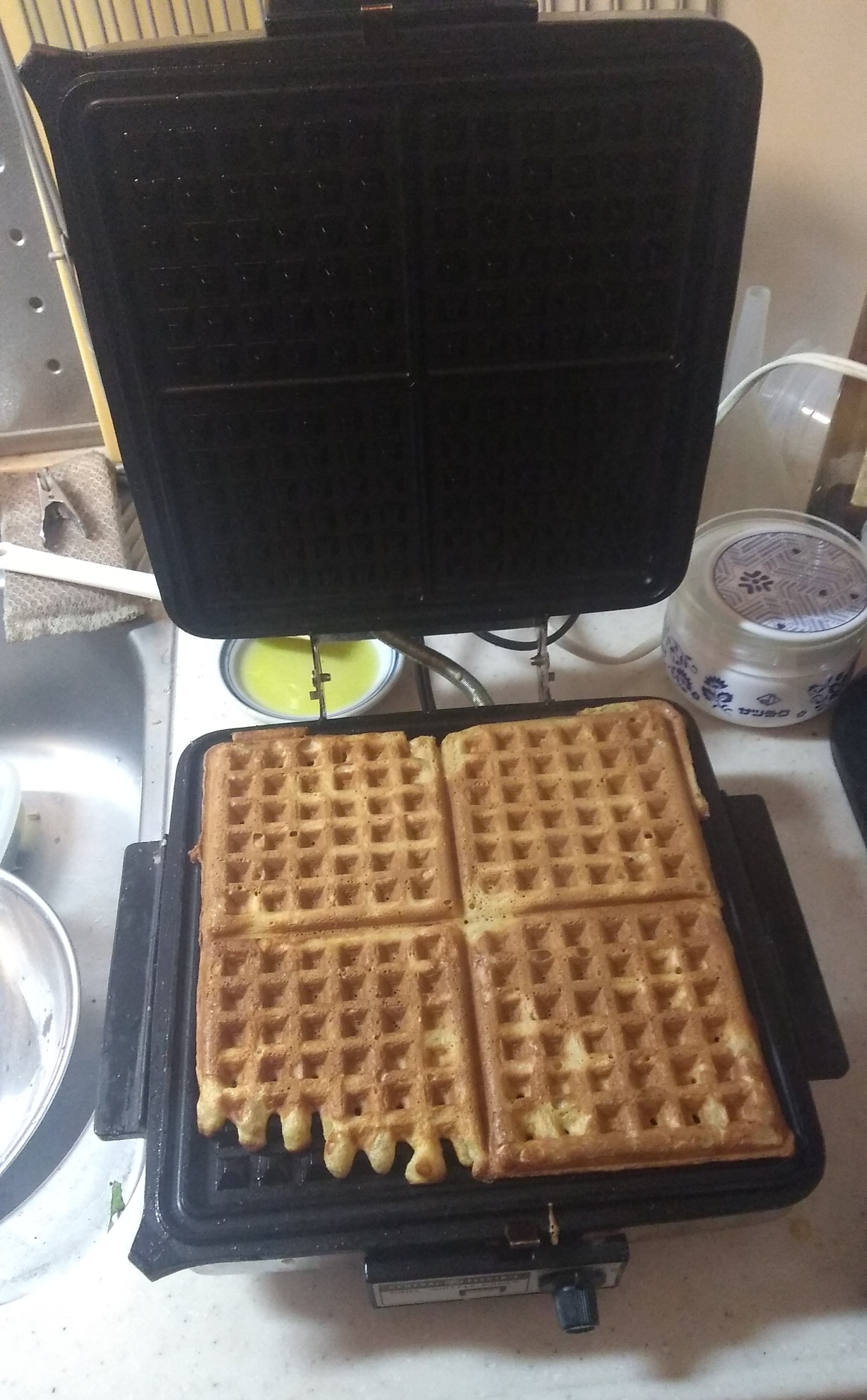 A stainless steel electric waffle iron by General Electric, open to reveal a baked waffle ready to lift out.