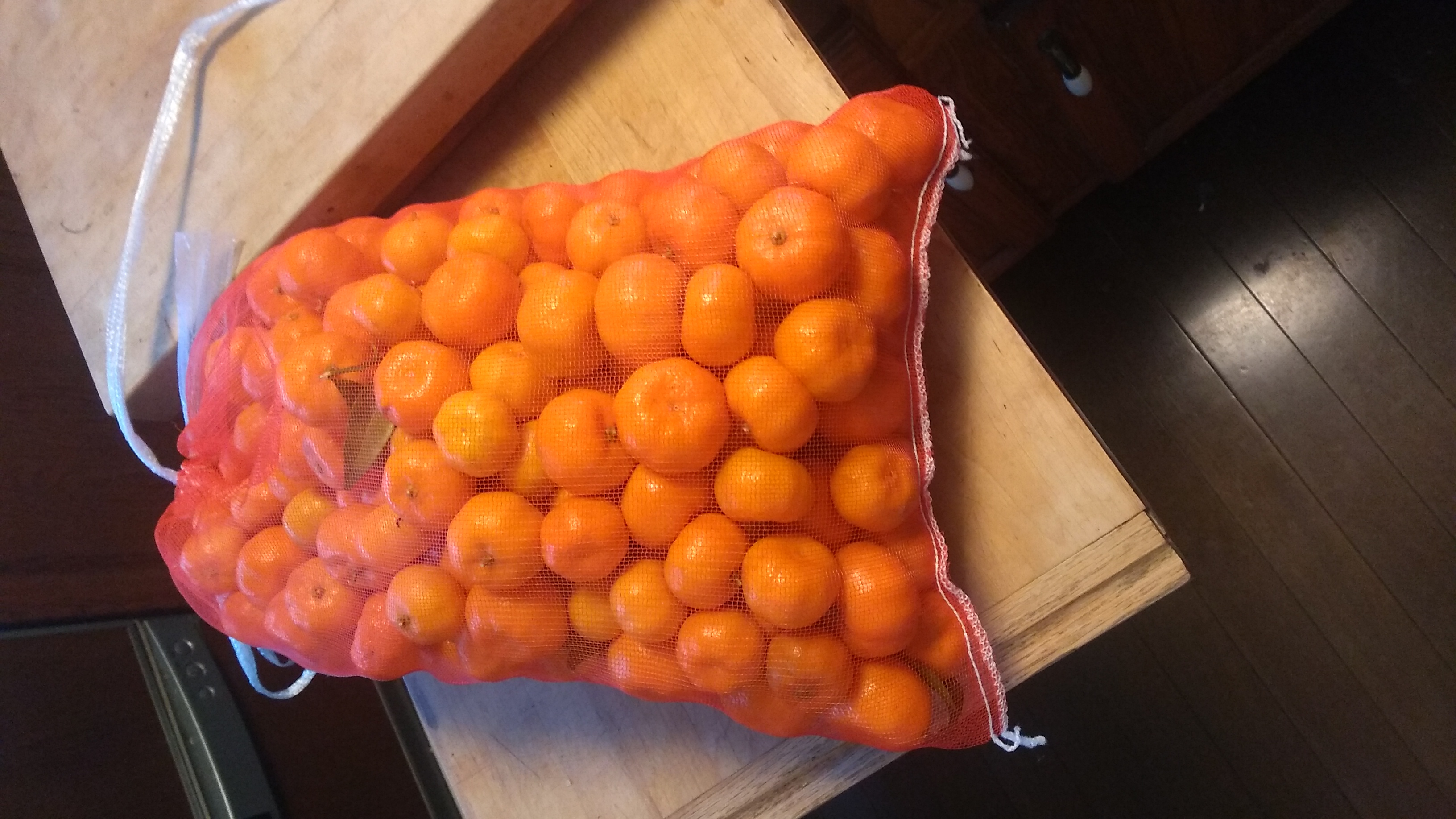 A net bag filled with shiikuasa fruit freshly cut from the tree, some with leaves still attached.